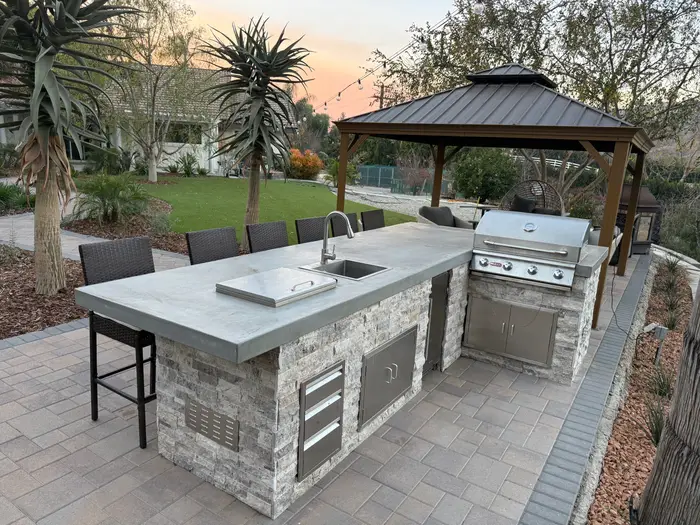 Stone outdoor kitchen island with grill and bar seating under a gazebo, La Habra