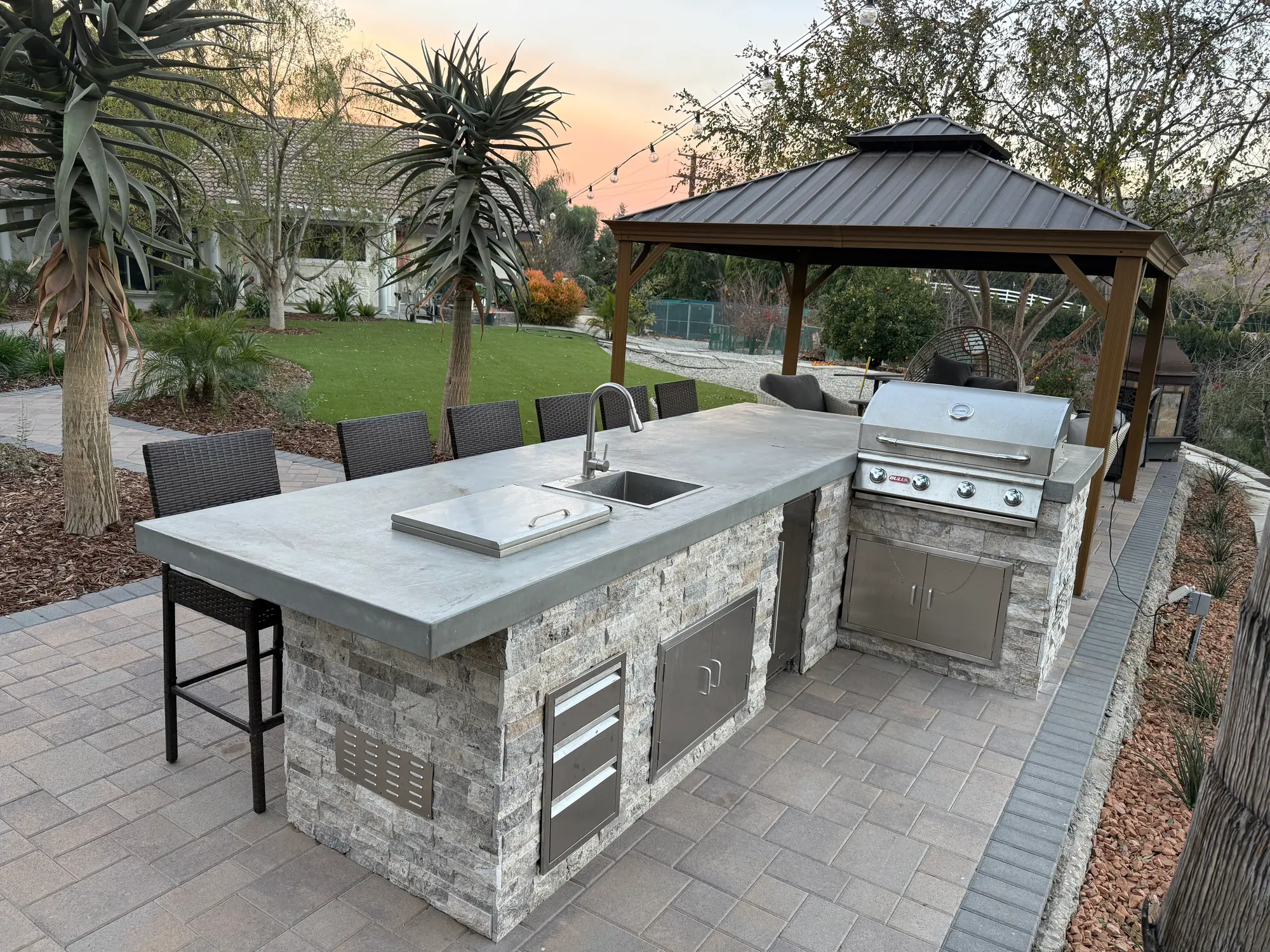 Stone outdoor kitchen island with grill and bar seating under a gazebo, La Habra